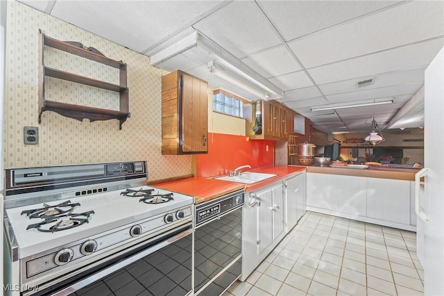 kitchen featuring a paneled ceiling, sink, light tile patterned floors, dishwashing machine, and range