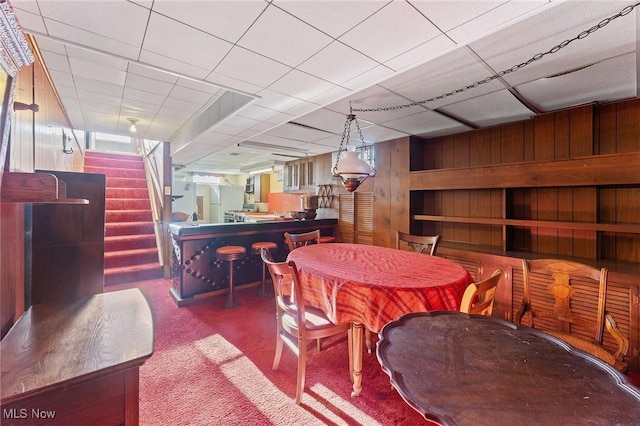 dining area featuring carpet flooring, a paneled ceiling, and wooden walls