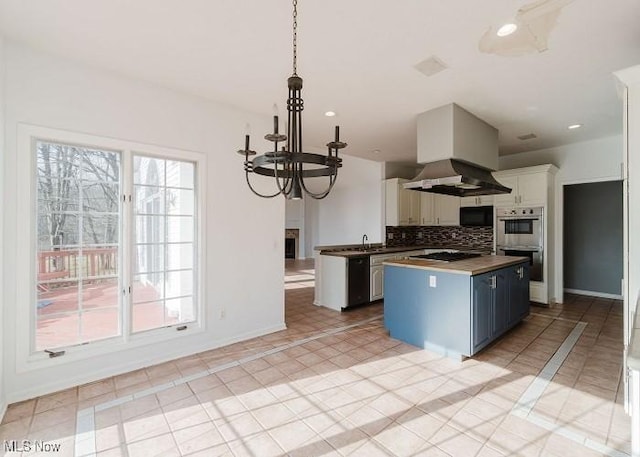 kitchen with decorative backsplash, wall chimney exhaust hood, blue cabinetry, white cabinets, and hanging light fixtures