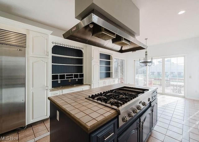 kitchen featuring appliances with stainless steel finishes, a kitchen island, exhaust hood, white cabinetry, and tile counters