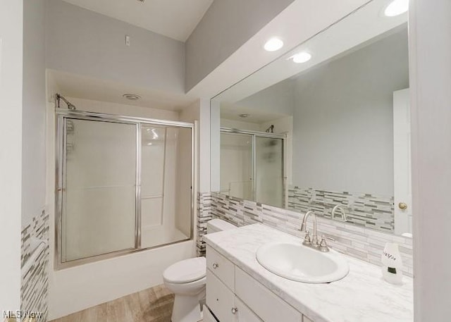 full bathroom with enclosed tub / shower combo, hardwood / wood-style floors, toilet, decorative backsplash, and vanity