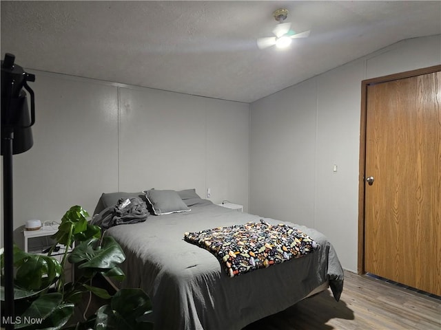 bedroom featuring a textured ceiling, light hardwood / wood-style floors, and lofted ceiling