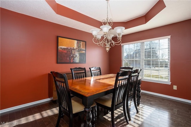 dining area featuring a raised ceiling, a healthy amount of sunlight, dark hardwood / wood-style flooring, and a chandelier