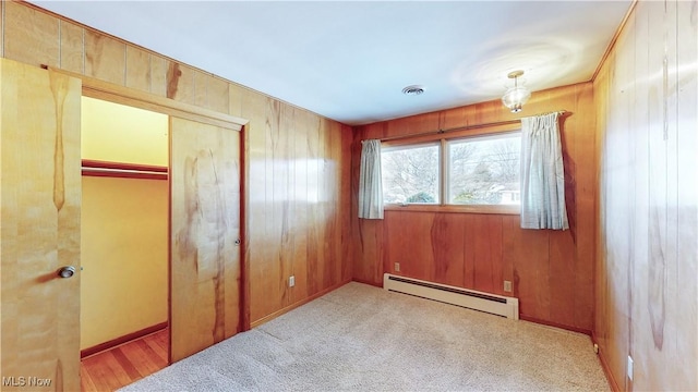 unfurnished bedroom featuring wooden walls, a closet, and a baseboard heating unit