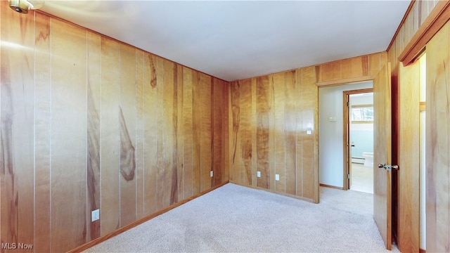 unfurnished room featuring light colored carpet, a baseboard radiator, and wood walls