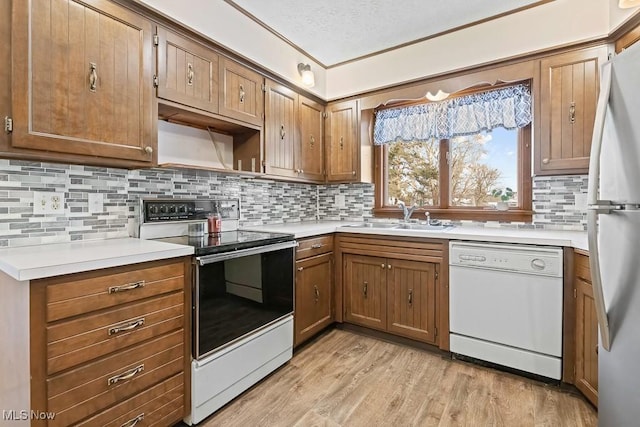 kitchen with tasteful backsplash, a textured ceiling, white appliances, sink, and light hardwood / wood-style floors