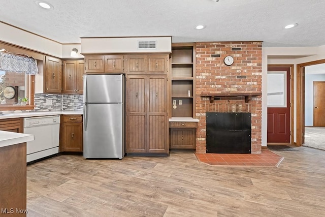 kitchen with stainless steel fridge, white dishwasher, a textured ceiling, a fireplace, and light wood-type flooring