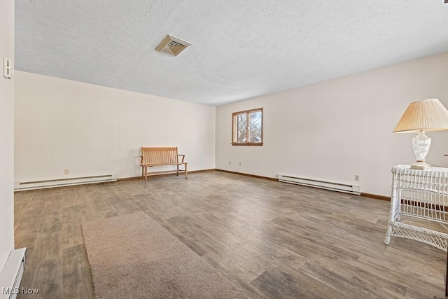 empty room featuring hardwood / wood-style floors, a textured ceiling, and a baseboard heating unit