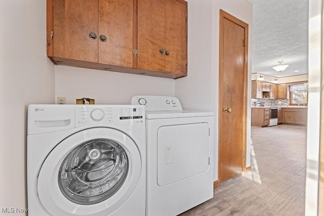 laundry area featuring light wood-type flooring, a textured ceiling, cabinets, and washing machine and clothes dryer