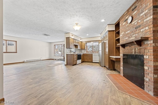 unfurnished living room featuring a textured ceiling, light hardwood / wood-style floors, a wealth of natural light, and a baseboard heating unit