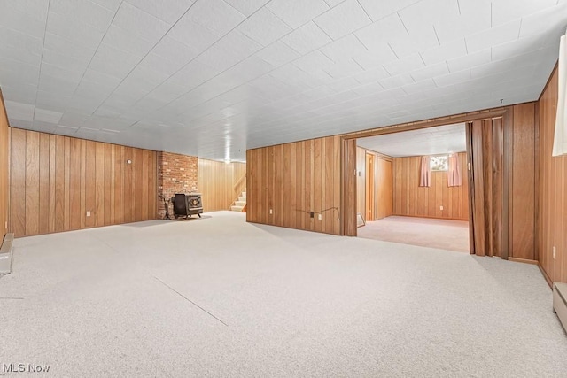 interior space with light colored carpet, a wood stove, wooden walls, and a baseboard heating unit