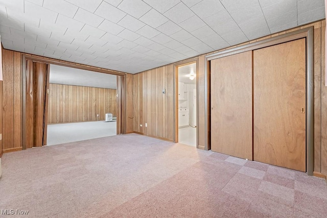 unfurnished bedroom featuring wooden walls, a closet, and light carpet