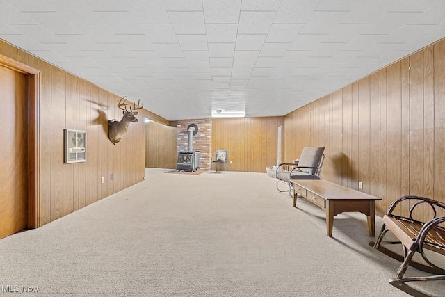 sitting room with a wood stove, wood walls, and carpet flooring