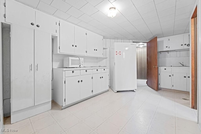 kitchen with white appliances, white cabinetry, and sink