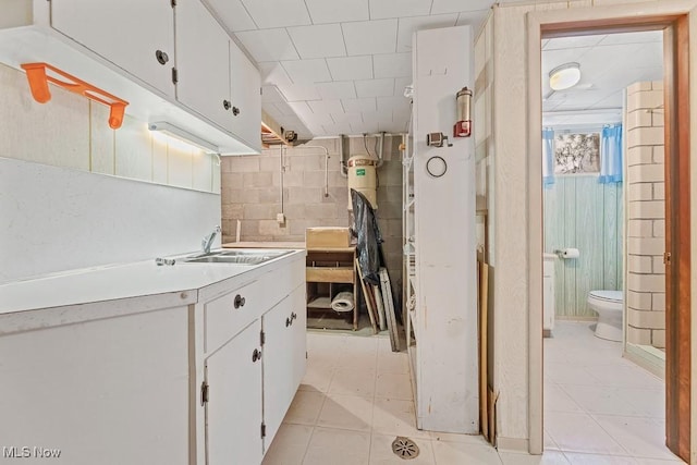 kitchen featuring white cabinetry, sink, light tile patterned flooring, and tile walls