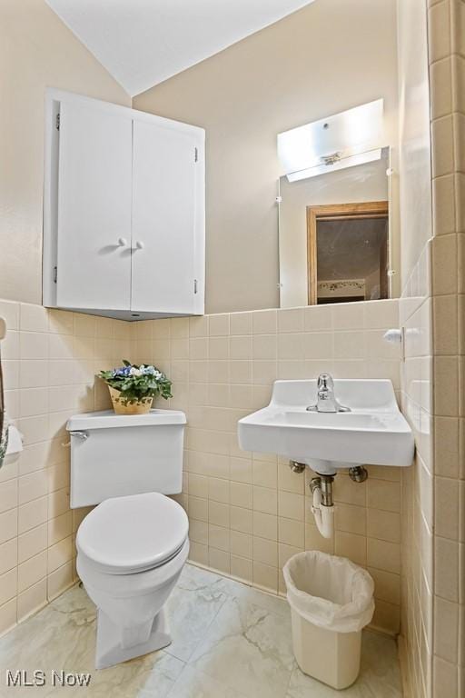 bathroom featuring lofted ceiling, sink, tile walls, and toilet