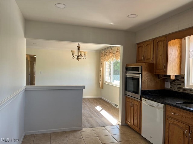 kitchen featuring stainless steel oven, an inviting chandelier, tasteful backsplash, white dishwasher, and light tile patterned floors