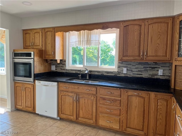 kitchen featuring dishwasher, stainless steel oven, sink, decorative backsplash, and light tile patterned floors