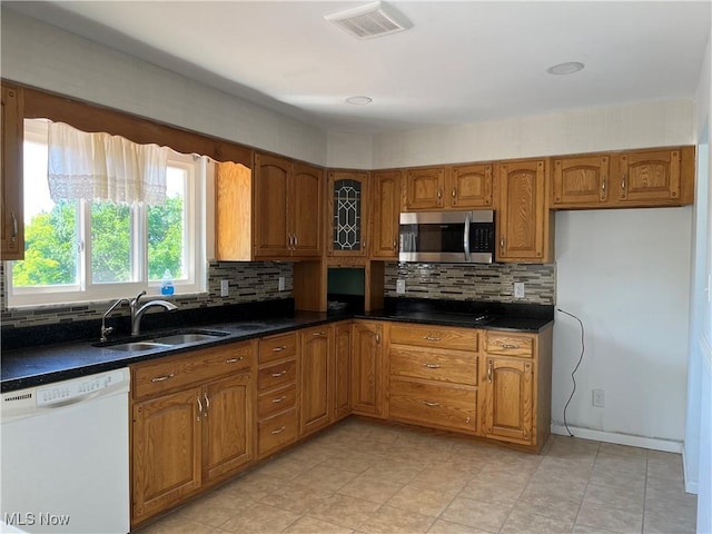 kitchen with white dishwasher, decorative backsplash, sink, and dark stone counters