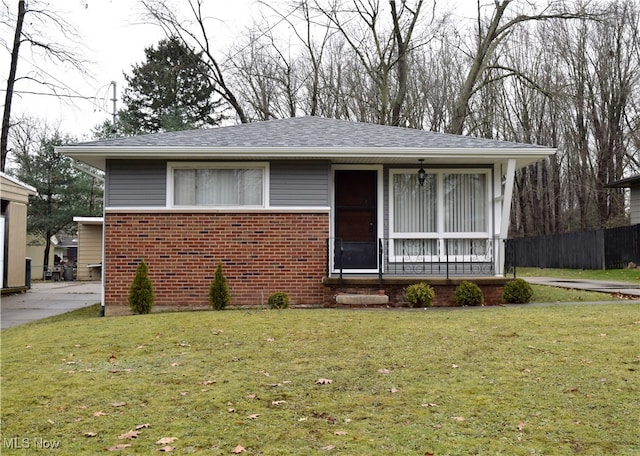 view of front of house featuring roof with shingles, brick siding, a front lawn, and fence