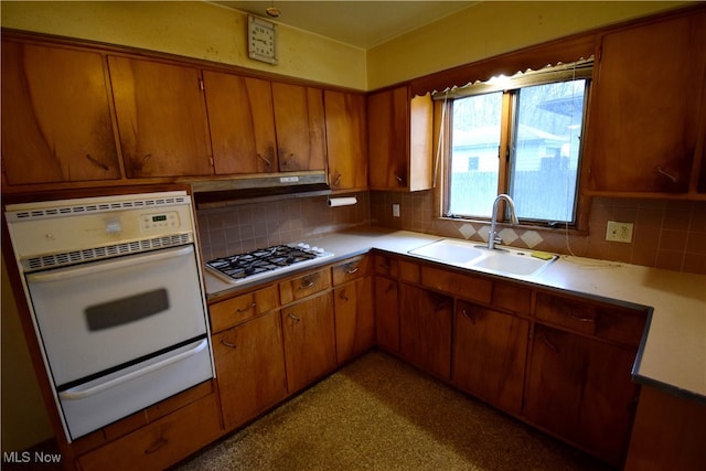 kitchen with stainless steel gas stovetop, decorative backsplash, sink, and white oven