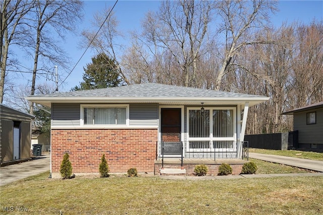 view of front facade with a front yard, fence, a porch, a shingled roof, and brick siding