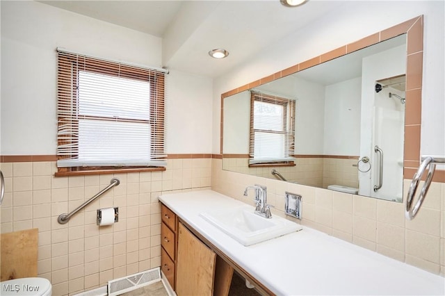 bathroom with a shower with door, a wainscoted wall, toilet, and tile walls