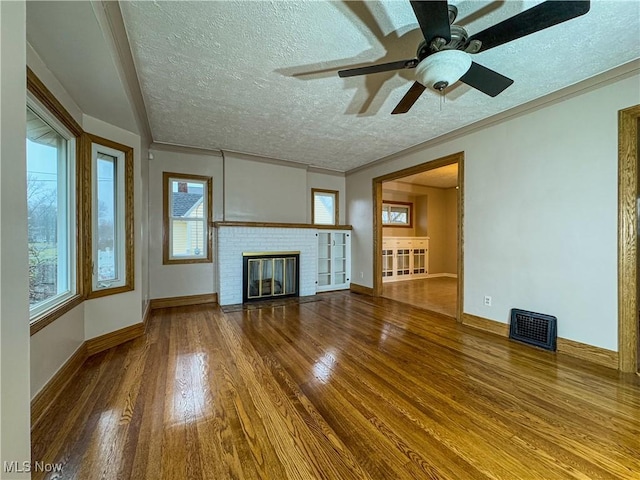 unfurnished living room featuring crown molding, hardwood / wood-style flooring, ceiling fan, a textured ceiling, and a brick fireplace