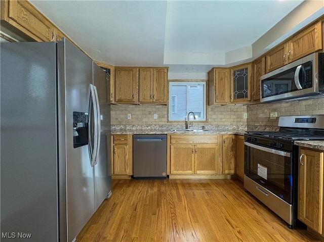 kitchen featuring sink, decorative backsplash, light stone counters, stainless steel appliances, and light wood-type flooring