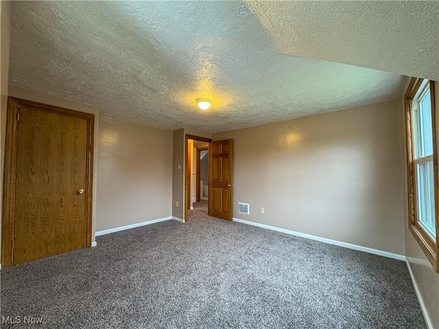 spare room featuring dark colored carpet and a textured ceiling