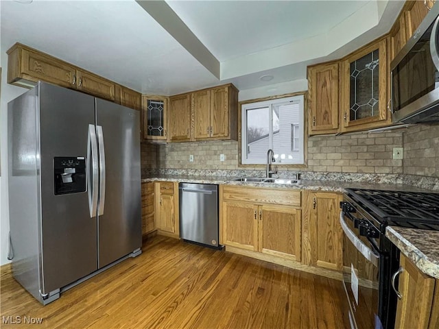 kitchen with tasteful backsplash, wood-type flooring, sink, light stone counters, and stainless steel appliances