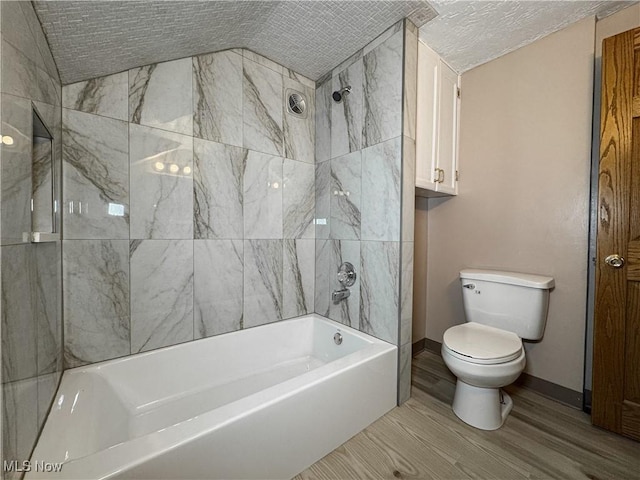 bathroom with hardwood / wood-style floors, tiled shower / bath combo, a textured ceiling, vaulted ceiling, and toilet