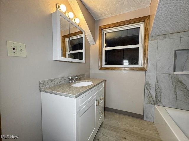 bathroom with vanity, a bathing tub, wood-type flooring, and a textured ceiling