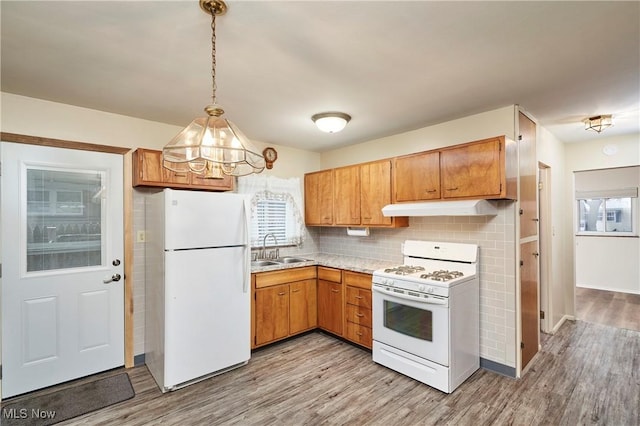 kitchen with pendant lighting, white appliances, backsplash, sink, and light wood-type flooring