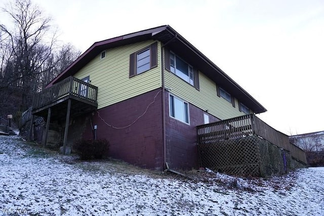 view of snowy exterior featuring a balcony and a wooden deck