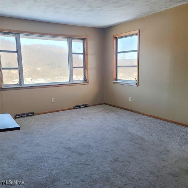 carpeted spare room featuring baseboards and visible vents