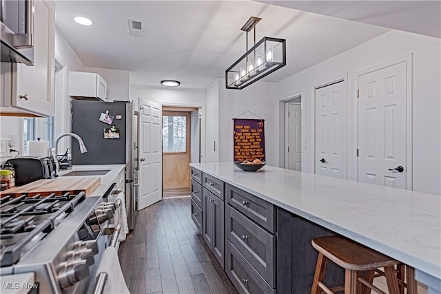 kitchen featuring light stone countertops, dark wood-type flooring, hanging light fixtures, a breakfast bar area, and white cabinets