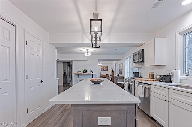 kitchen with stainless steel appliances, a kitchen island, pendant lighting, hardwood / wood-style floors, and white cabinetry