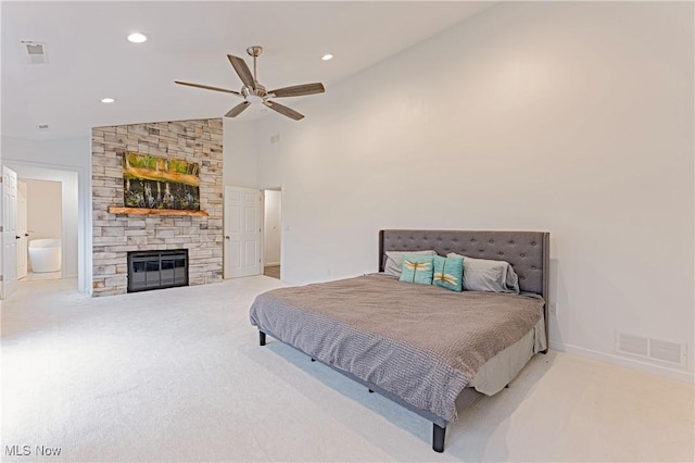 bedroom featuring connected bathroom, ceiling fan, a stone fireplace, high vaulted ceiling, and light carpet