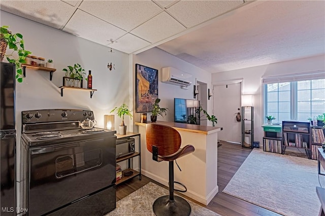 kitchen with dark hardwood / wood-style floors, a drop ceiling, black range with electric stovetop, and an AC wall unit