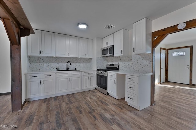 kitchen featuring appliances with stainless steel finishes, backsplash, sink, white cabinets, and light hardwood / wood-style floors