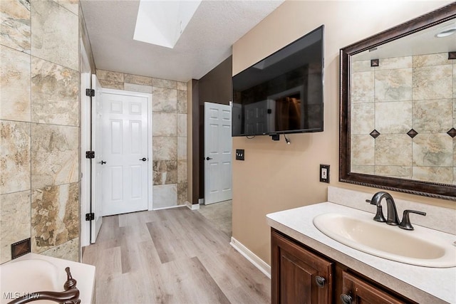 bathroom featuring hardwood / wood-style floors, vanity, a skylight, a textured ceiling, and tile walls