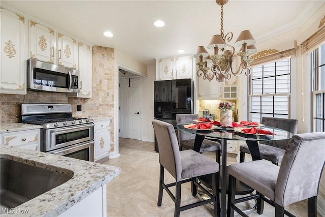 kitchen with white cabinets, stainless steel appliances, tasteful backsplash, light stone counters, and a notable chandelier