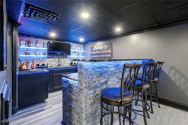 bar with a paneled ceiling, light hardwood / wood-style floors, sink, and dark stone counters