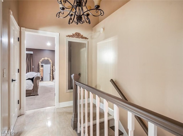 corridor with baseboards, a notable chandelier, and an upstairs landing