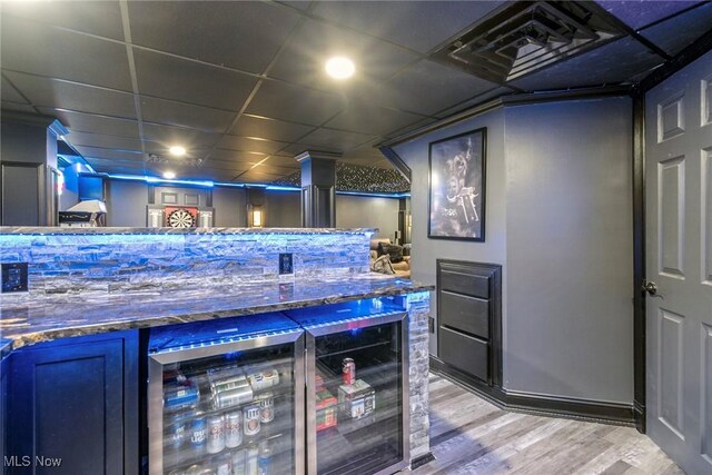 bar featuring light wood-style flooring, a drop ceiling, and beverage cooler