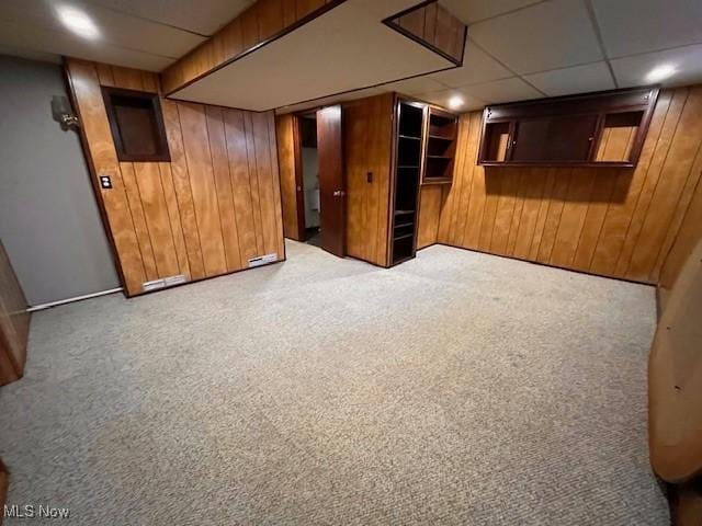 carpeted spare room with wooden walls and a paneled ceiling