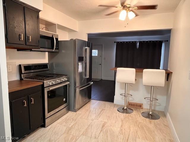 kitchen featuring dark brown cabinets, ceiling fan, stainless steel appliances, and a breakfast bar area