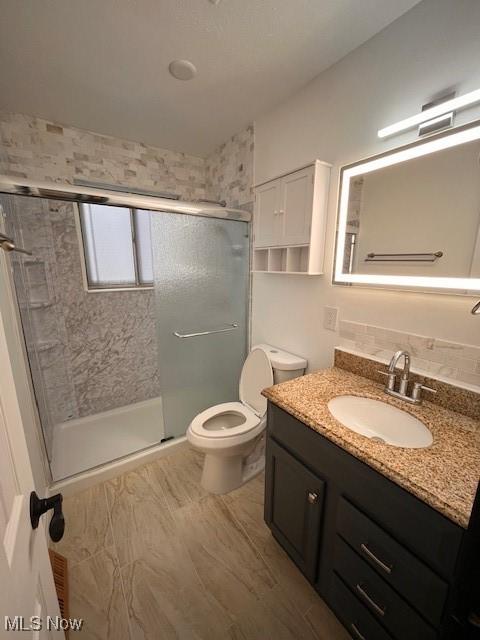 bathroom featuring vanity, tasteful backsplash, an enclosed shower, and toilet