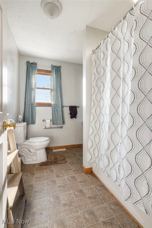 bathroom with shower / tub combo, a textured ceiling, and toilet